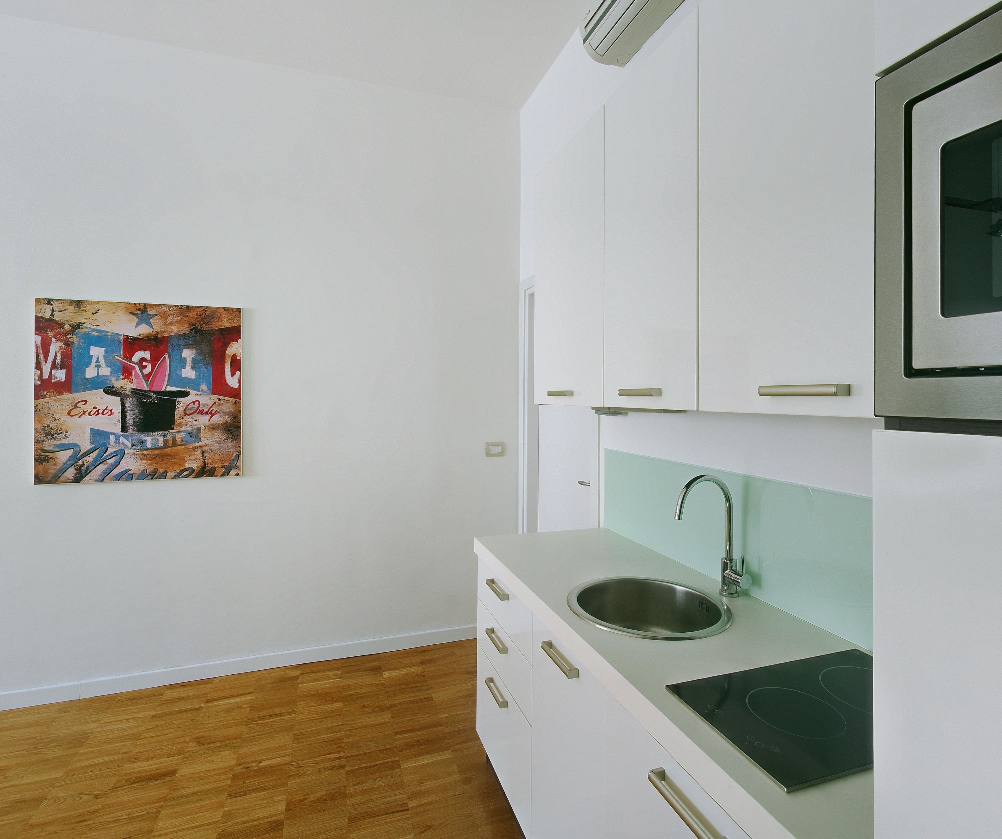 Uma cozinha moderna com armários brancos, uma pia de aço inoxidável e uma placa de indução.