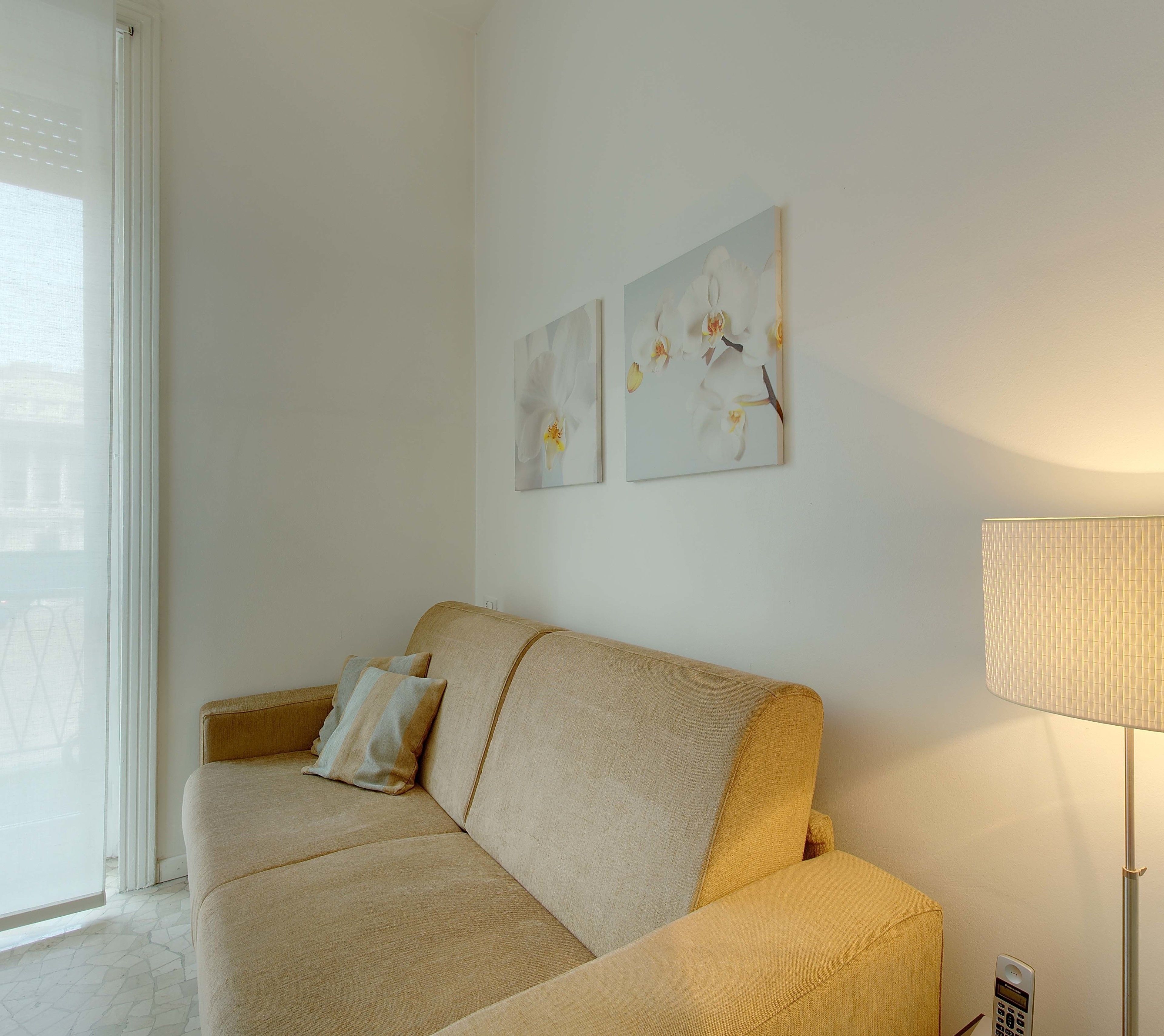 A living room with a beige sofa, two pillows, and two wall-mounted paintings of flowers.