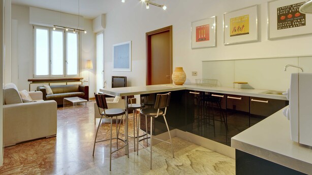 A modern kitchen with a central island, bar stools, and a dining area with a sofa and chairs.