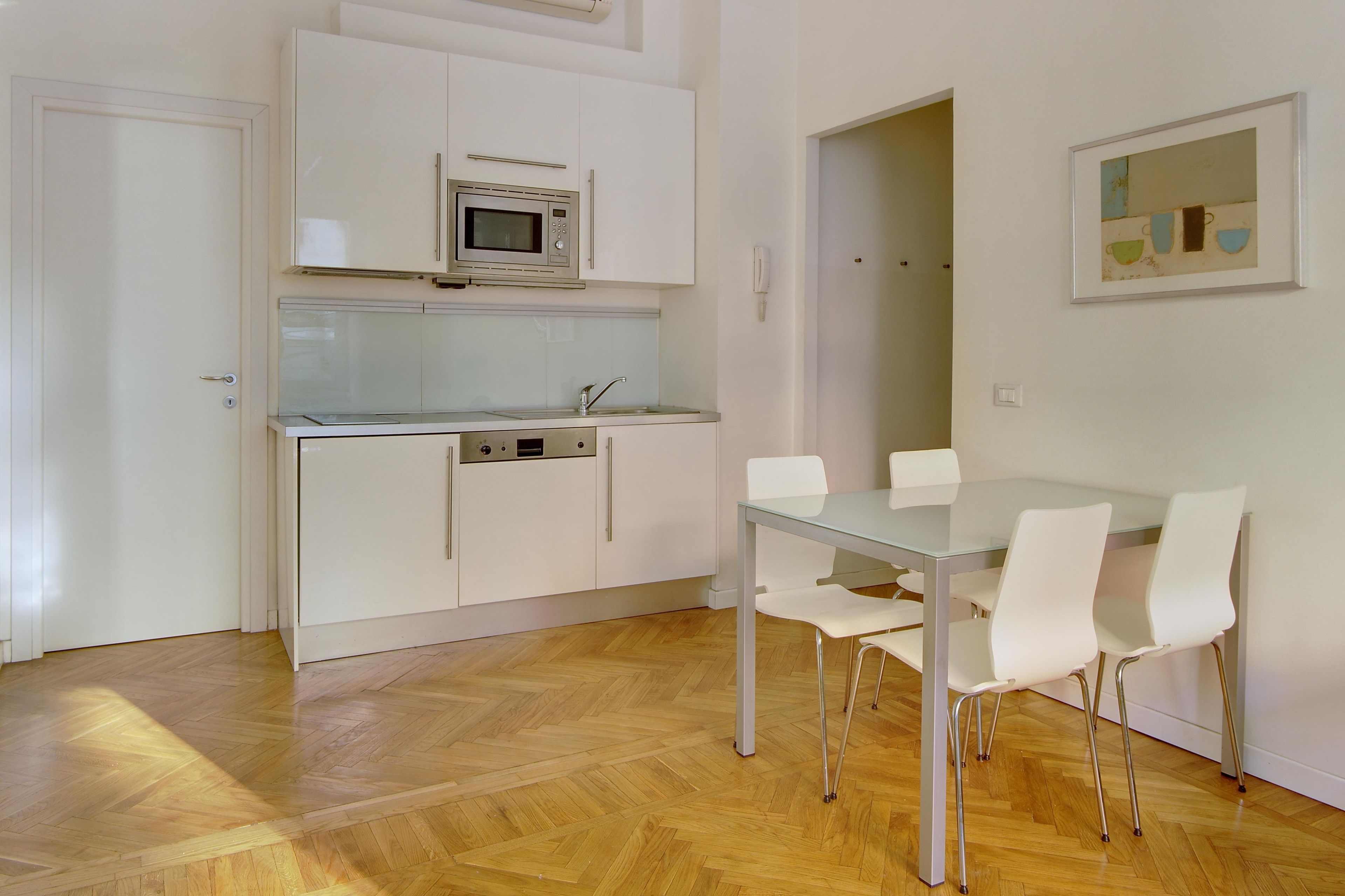 A modern kitchen with white cabinets, a microwave, and a glass-top dining table with white chairs.