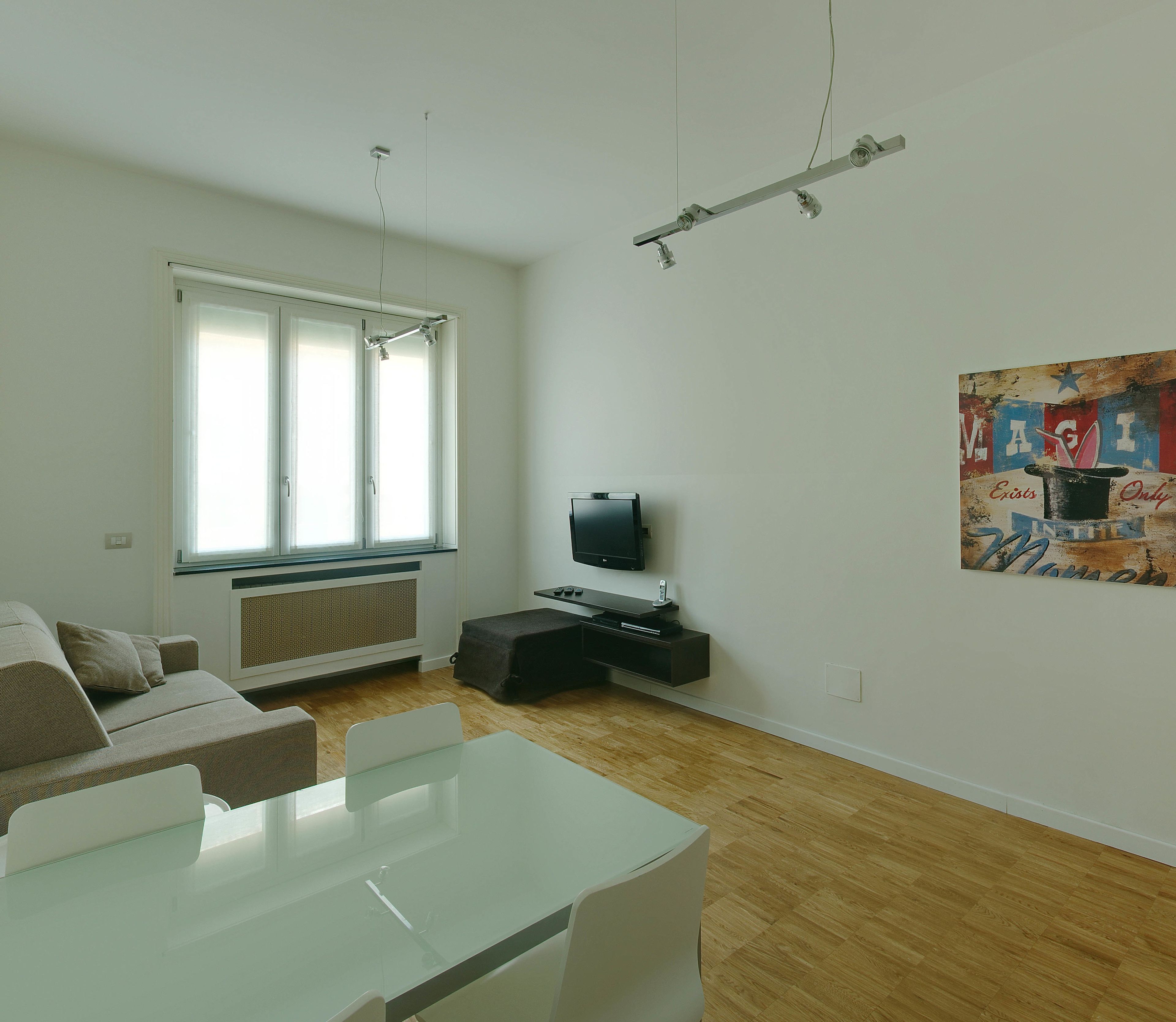 Una sala de estar moderna con un sofá, una mesa de centro de vidrio, un televisor de pantalla plana y un cuadro en la pared.