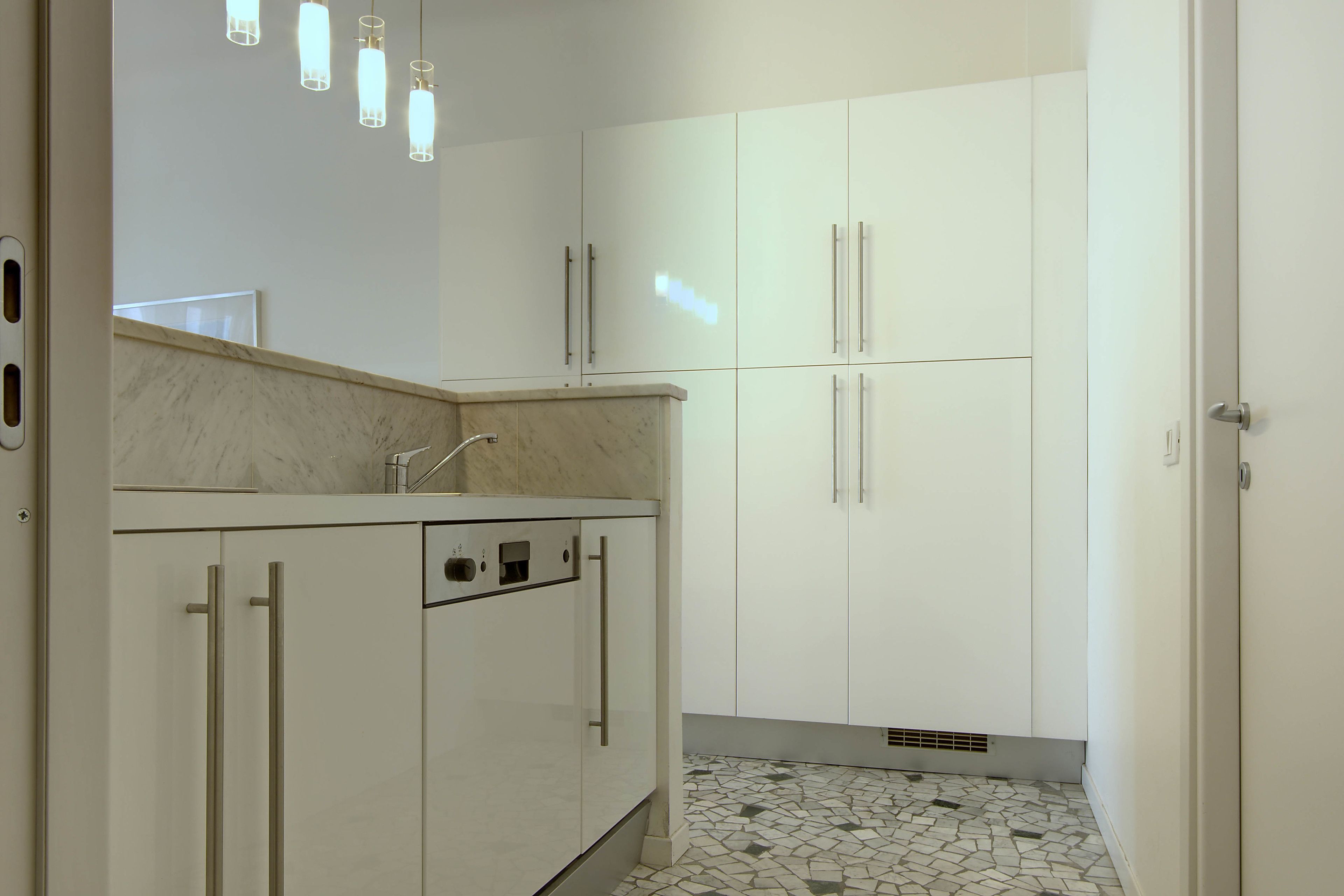A modern kitchen with white cabinets, a marble countertop, and a tiled backsplash.