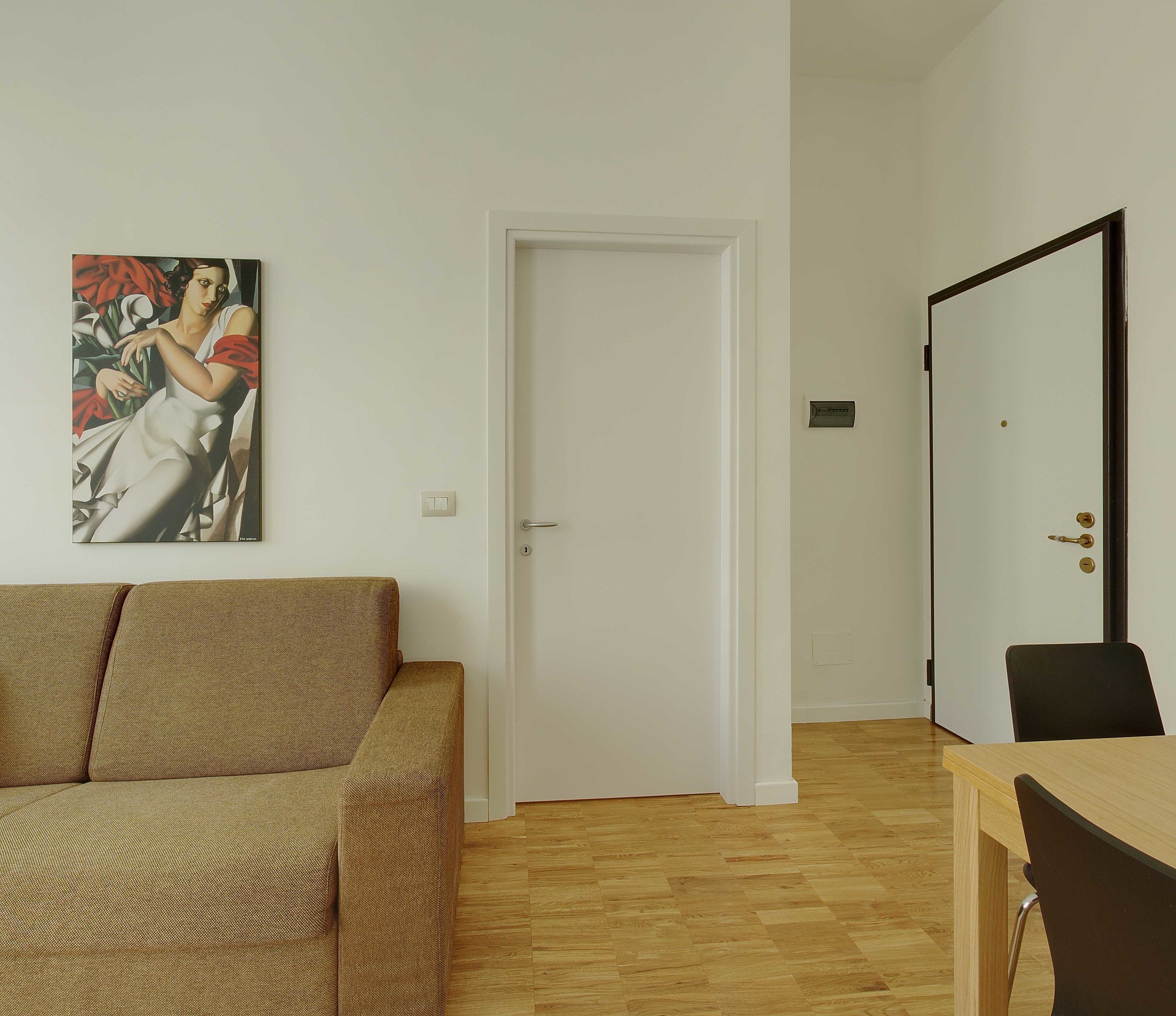 Un salon avec un canapé beige, une table à manger avec deux chaises, une porte blanche et un tableau accroché au mur.
