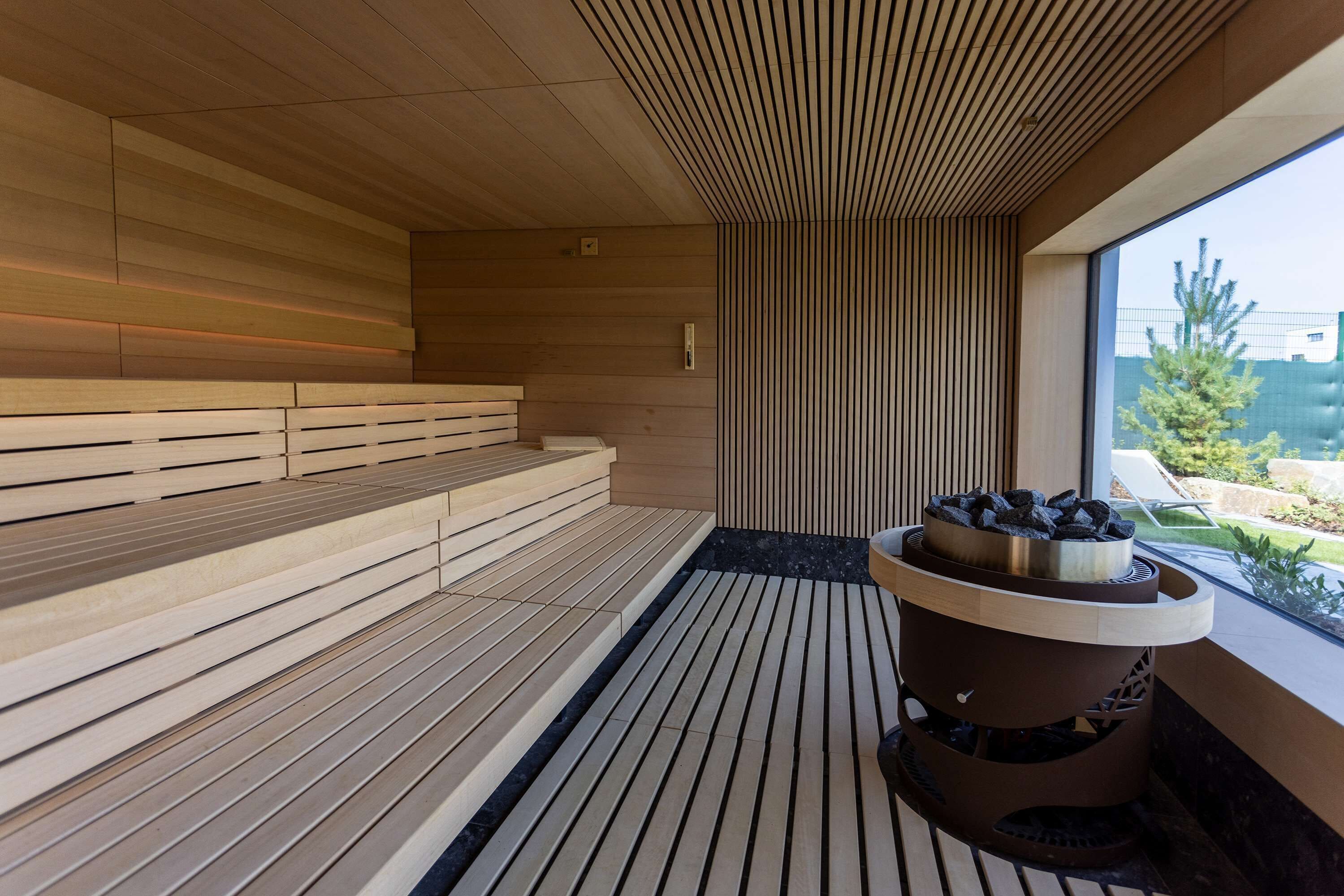 A modern sauna with wooden benches and a central heated stone feature.