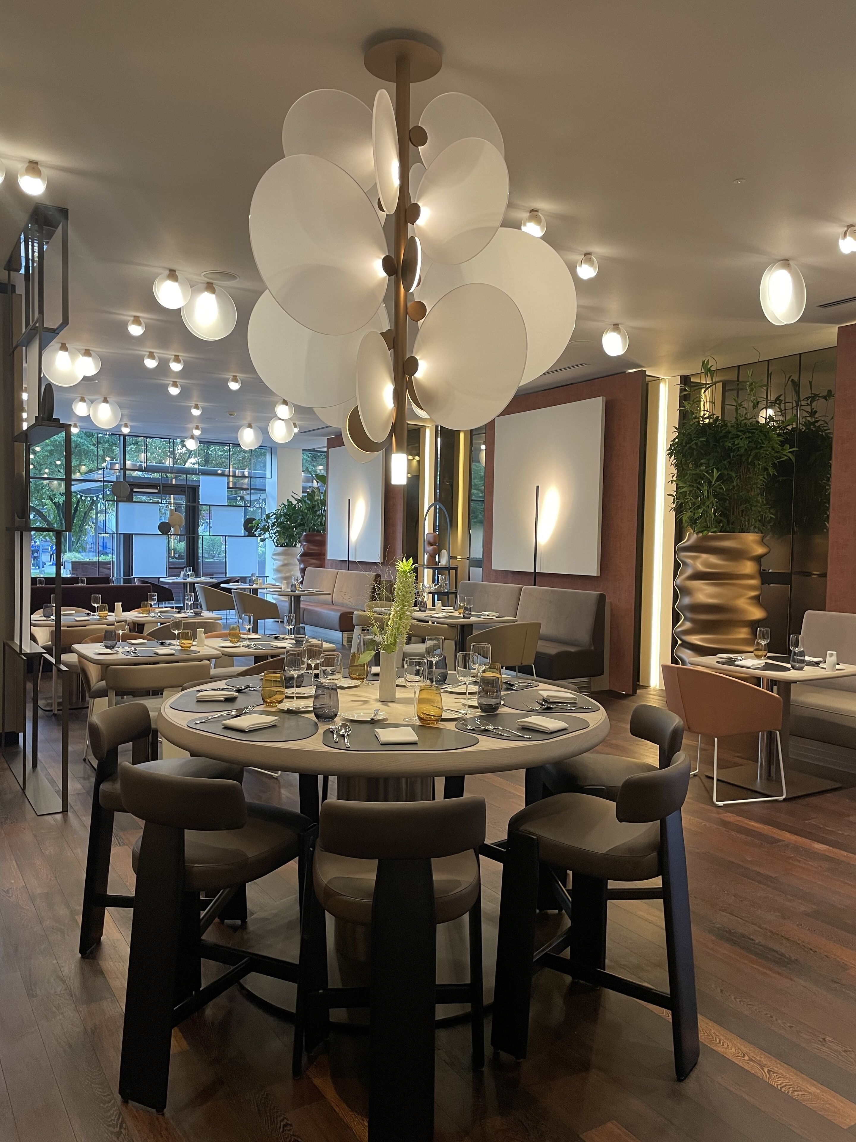 A modern dining area with round tables, dark chairs, and a unique ceiling light fixture.