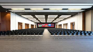 Ein Konferenzraum mit Reihen von Stühlen, einem großen Bildschirm an der Front und einem Teppichboden.