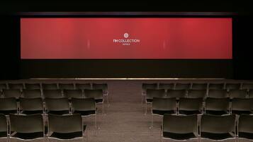 An empty auditorium with rows of chairs facing a large screen displaying "NH COLLECTION HOTELS".