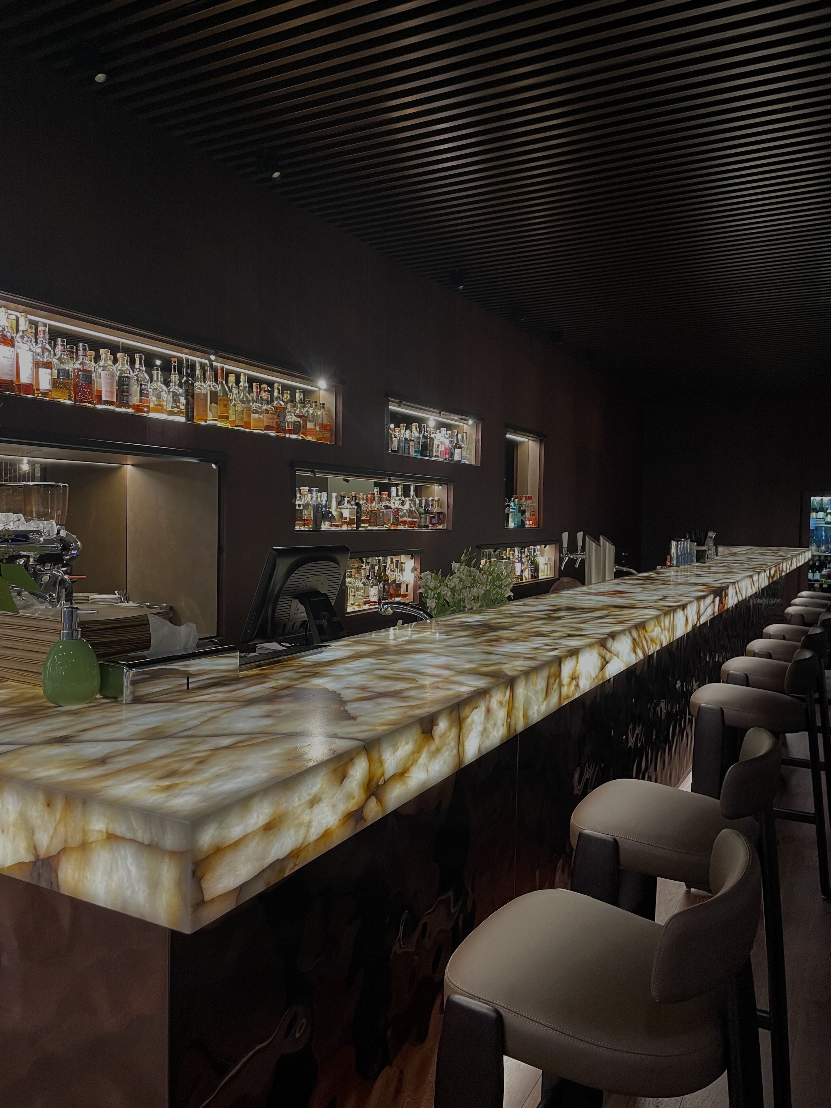 Un espace bar doté d’un long comptoir, de nombreuses étagères remplies de bouteilles et de tabourets de bar.