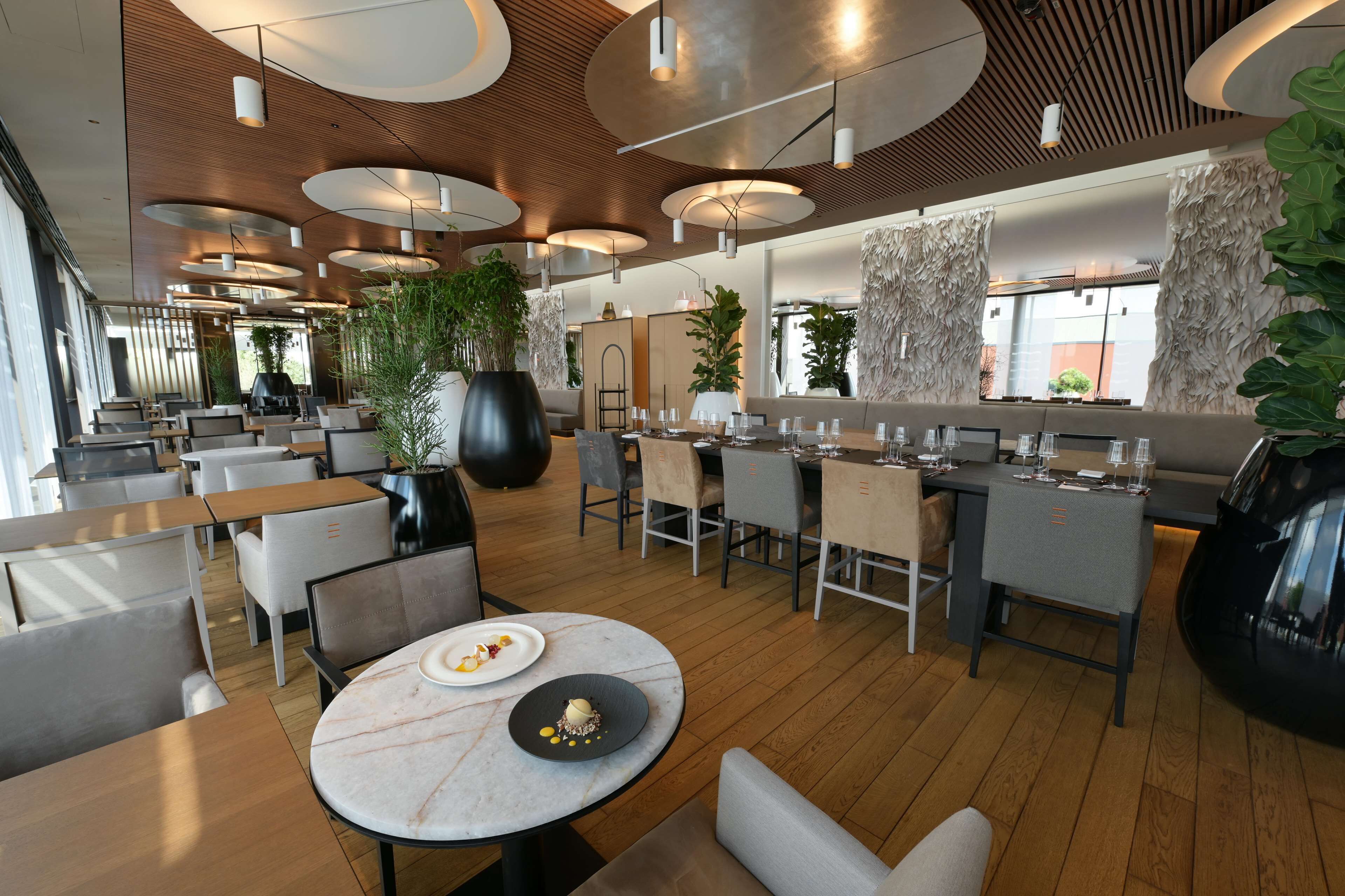 Un restaurant moderne avec des tables rondes, des chaises et une variété de plantes.