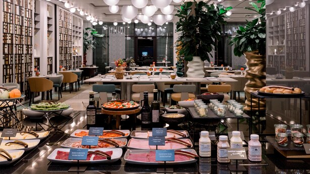Un buffet proposant une variété de plats, un espace pour s’asseoir et une grande plante au centre.