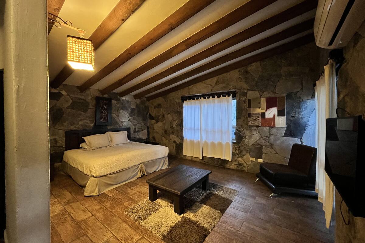 A cozy bedroom with a stone wall, a bed, a wooden bench, and a stone fireplace.
