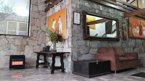 A stone-walled lobby with a brown leather sofa, a small table with a vase, and a heater. - Hotel Chipinque (San Pedro Garza García)