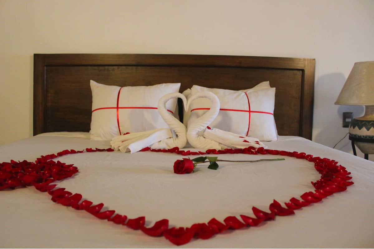 A bed with a heart-shaped arrangement of rose petals and towels.
