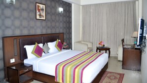 A hotel room with a large bed, a nightstand, a desk, a chair, a TV, and a window with curtains.