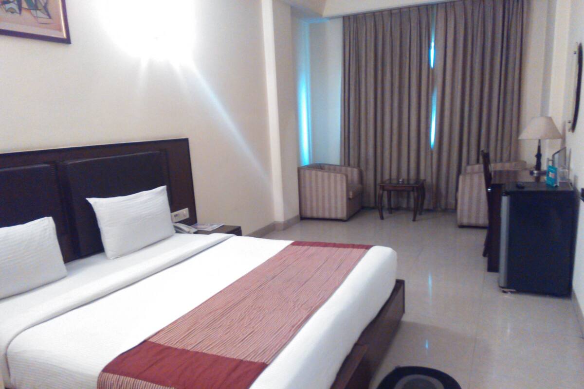 A hotel room with a large bed, a desk, a chair, and a view of the outside through a window.