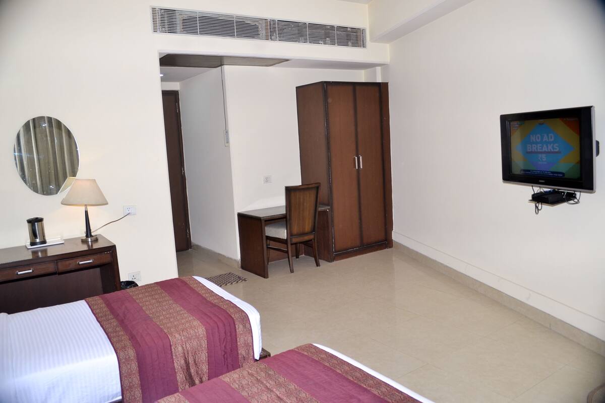 A hotel room with a bed, a desk, a wardrobe, a television, and a mirror.