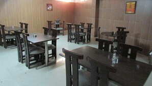 A dining area with multiple tables and chairs, wooden panel walls, and ceiling lights.