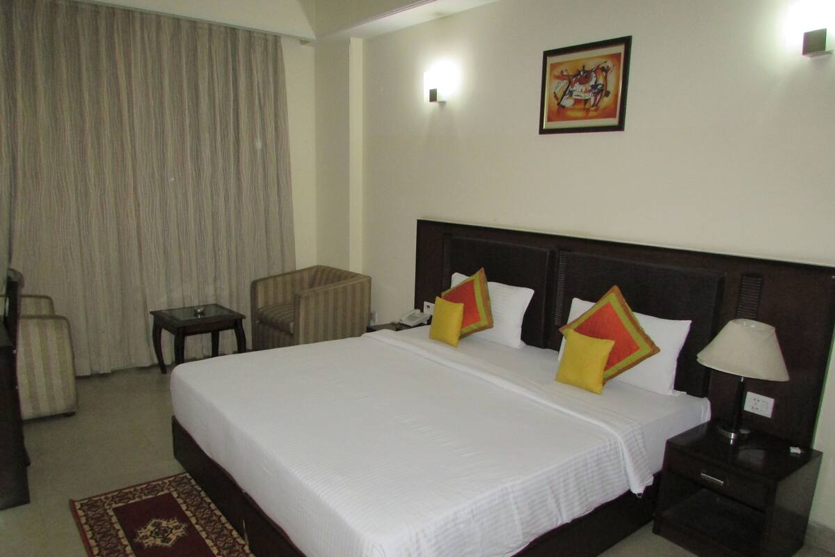 A hotel room with a large bed, two bedside tables, a chair, a desk, and a lamp.