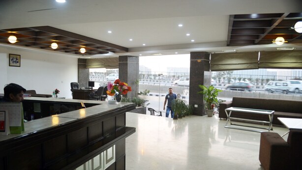 A modern lobby with a reception desk, seating area, and large windows offering a view of the street.