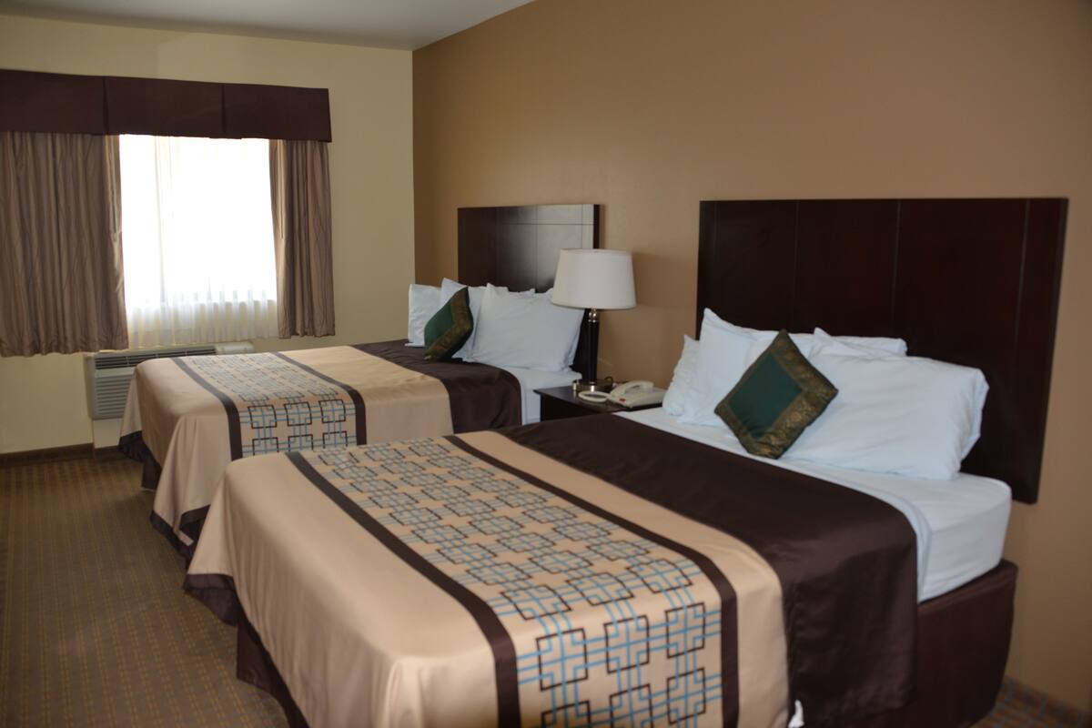 A hotel room with two beds, a nightstand with a lamp, and a window with curtains.