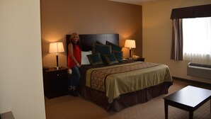 Una habitación de hotel con una cama, dos mesitas de noche con lámparas, una mesita auxiliar y una ventana con cortinas, además de un aire acondicionado.
