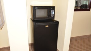 Un refrigerador negro compacto con un microondas encima, ubicado en un pasillo estrecho con piso estampado.