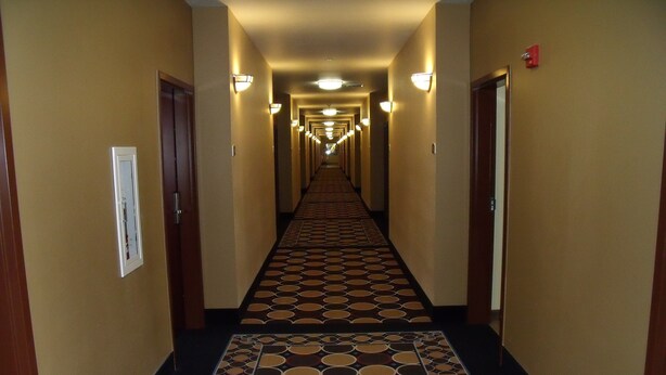 Un pasillo de hotel con alfombra estampada, puertas a ambos lados y luces empotradas en la pared.