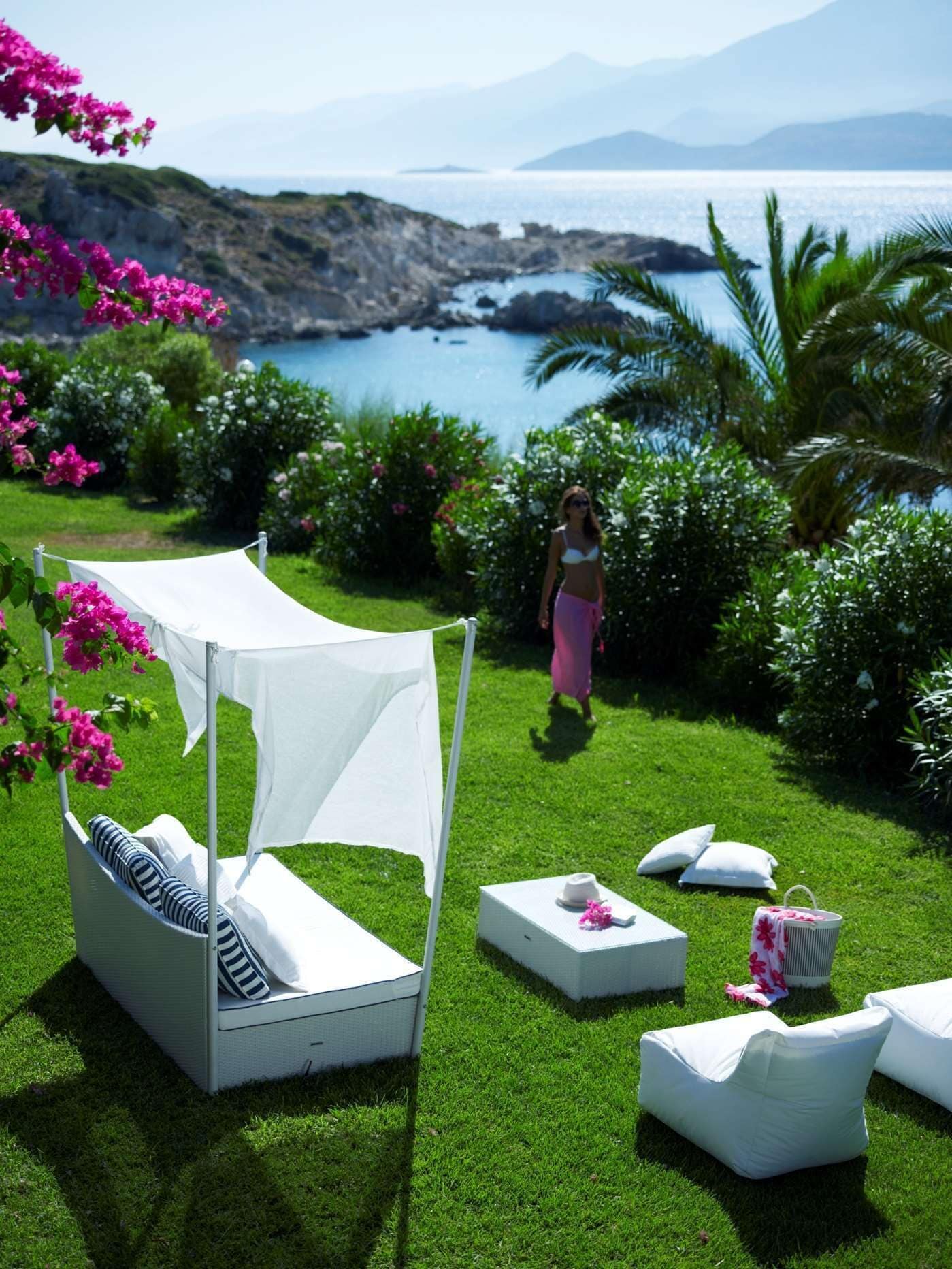 A garden with a white canopy seating area, white cushions, and a small table with a hat and flowers.