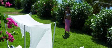 A garden with a white canopy seating area, white cushions, and a small table with a hat and flowers.