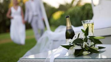 Ein Glastisch mit einer Champagnerflasche und einem Glas Weißwein, ein Strauß weißer Blumen und eine weiße Tischläufer.