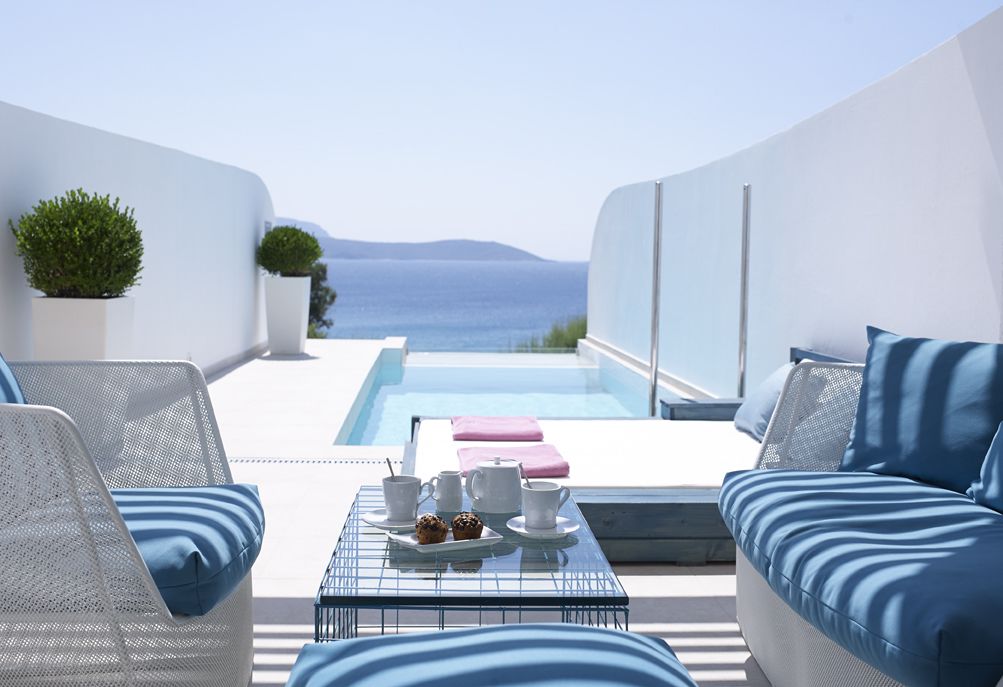 Un área de estar moderna al aire libre con piscina, paredes blancas y vista al mar.