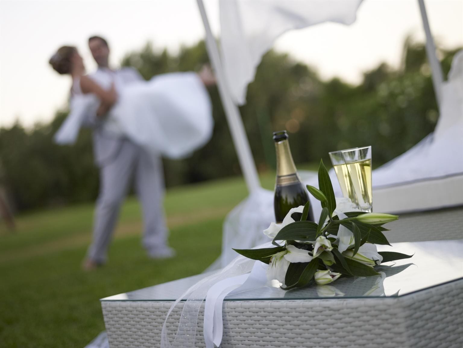 Eine Hochzeitsszene mit einem Paar im Hintergrund und einem Tisch mit einer Flasche und Gläsern im Vordergrund.