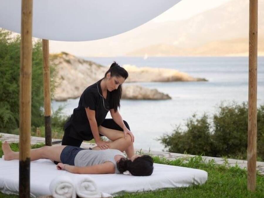A person receiving a massage outdoors with a scenic view of the sea and hills in the background.