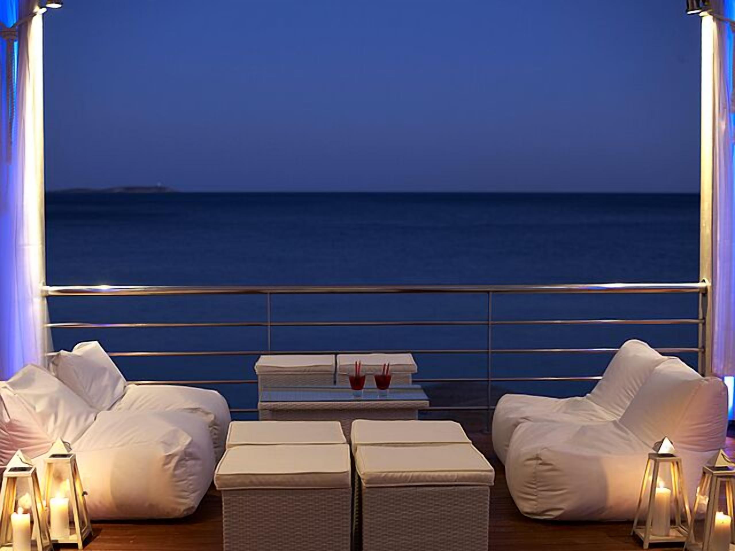 Een balkon met wit beklede zitting en een kleine tafel, met uitzicht op de zee.