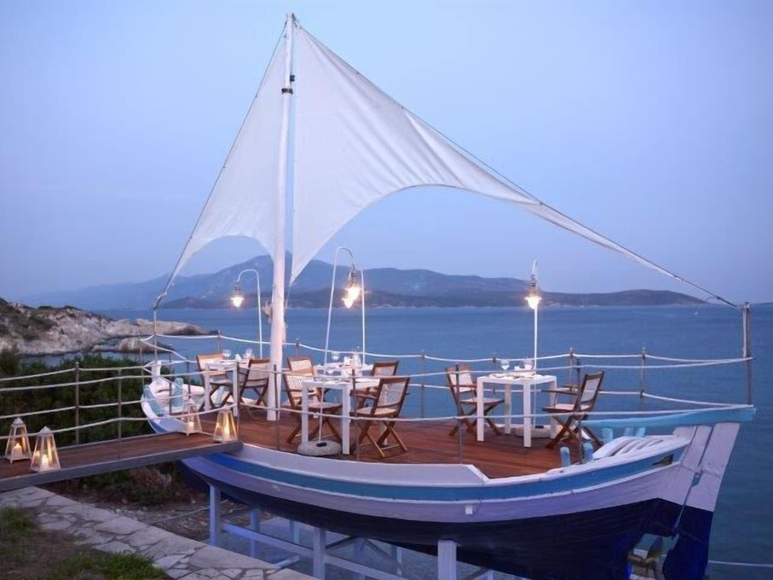 An outdoor dining area on a boat with tables and chairs, surrounded by a white canopy, overlooking a body of water with distant land.