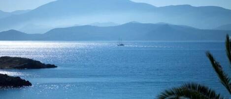 A coastal view with a boat on the water, mountains in the background, and some vegetation in the foreground.