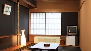 Una habitación tradicional japonesa con suelo de tatami, una mesa baja, un televisor y un calentador.