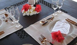 A table set with white plates, silverware, and clear glasses, accompanied by red and white flowers. - Tijara Beach (Mombasa)