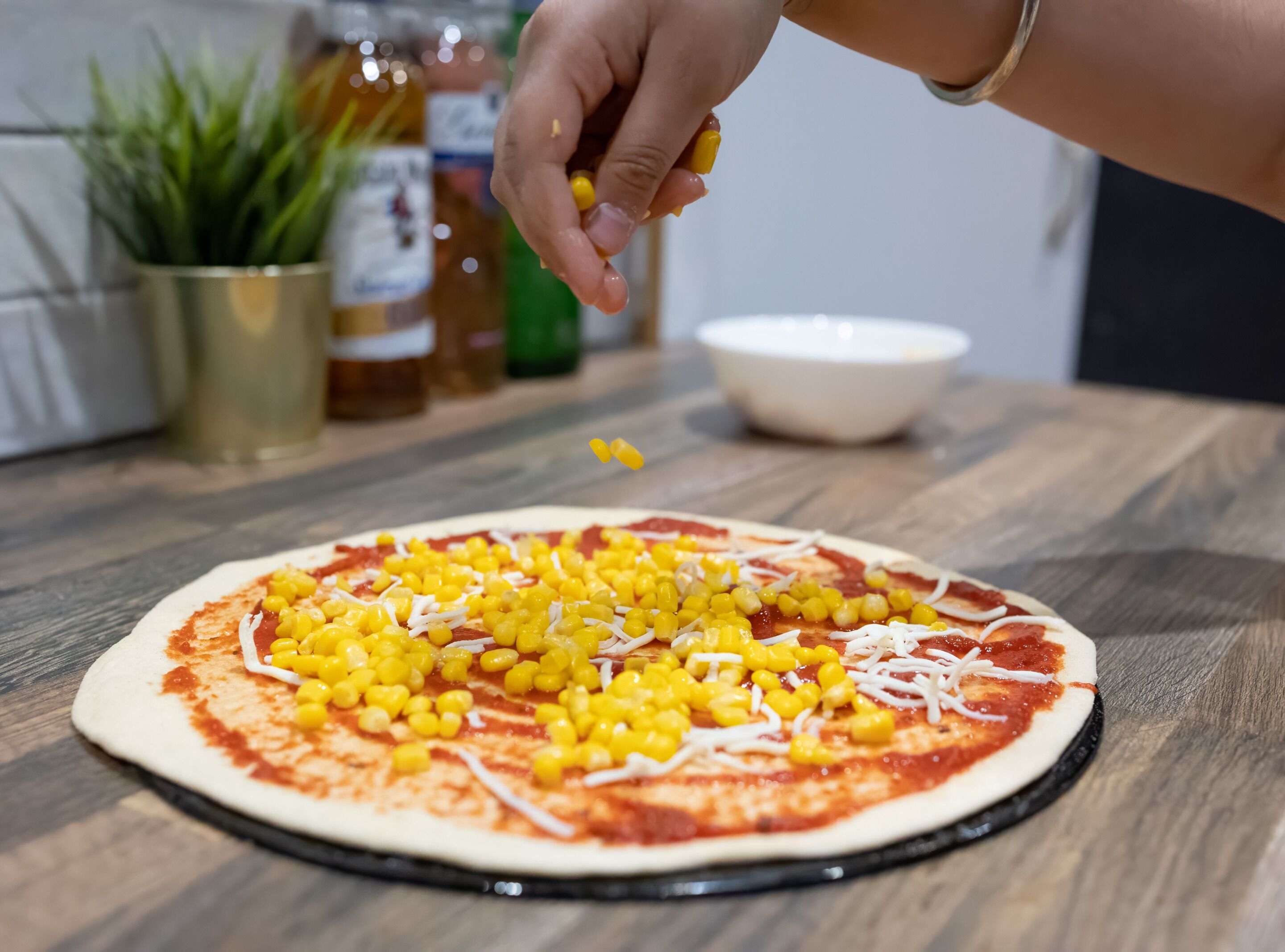Une pizza en cours de préparation, garnie de grains de maïs et de fromage, sur une table en bois.