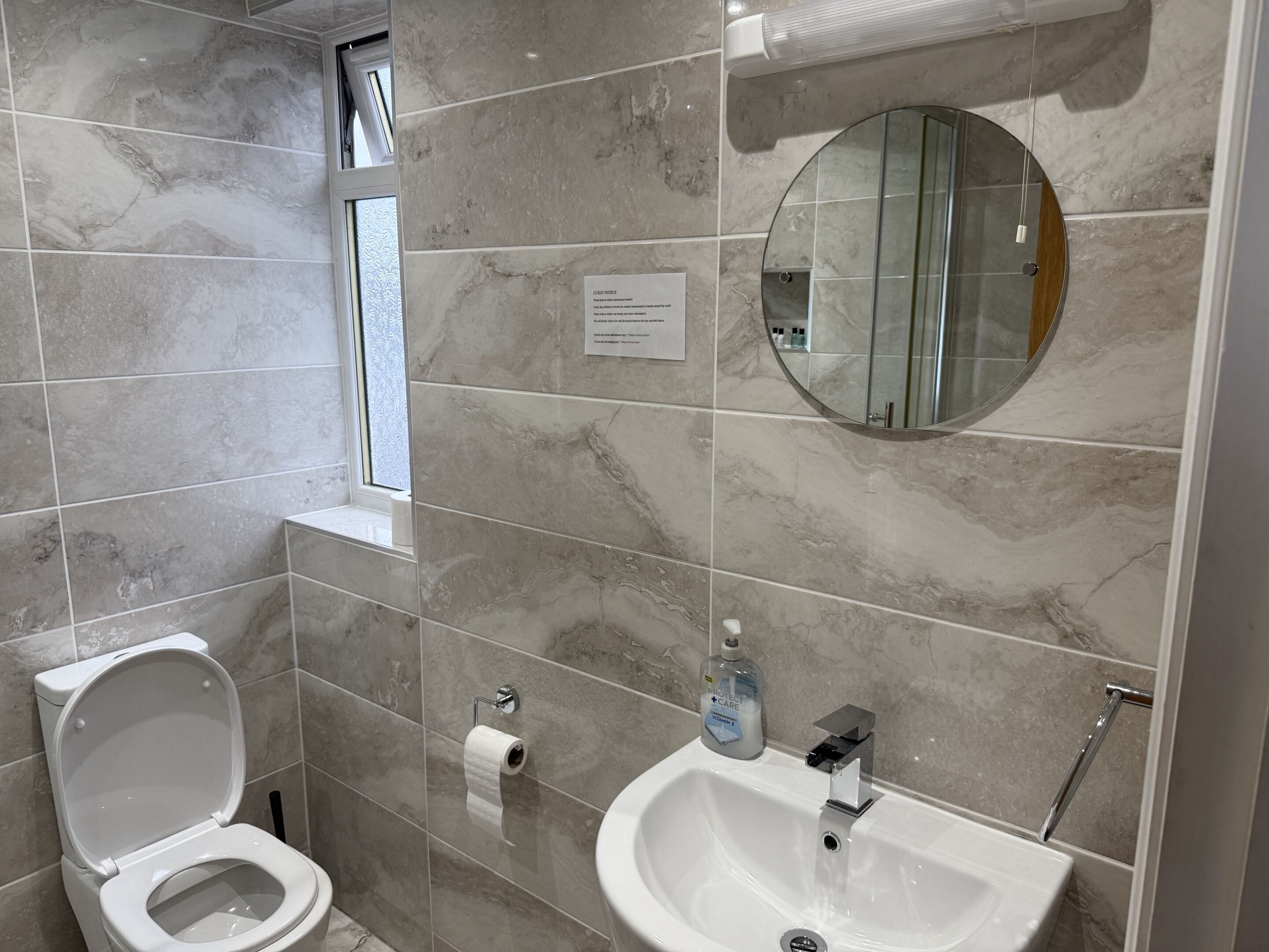 Une salle de bain avec des toilettes, un lavabo, un miroir et une fenêtre.