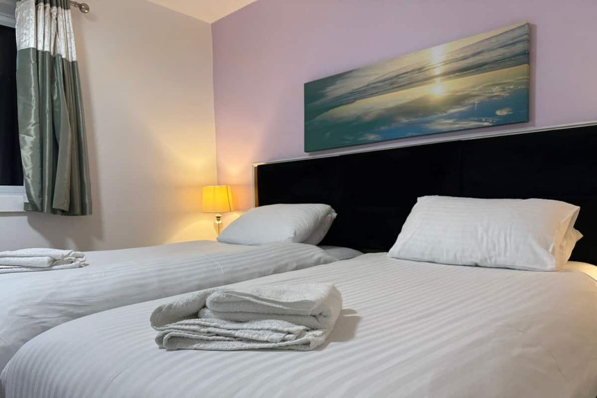 Quarto de hotel com duas camas, um quadro na parede e uma janela com cortinas.