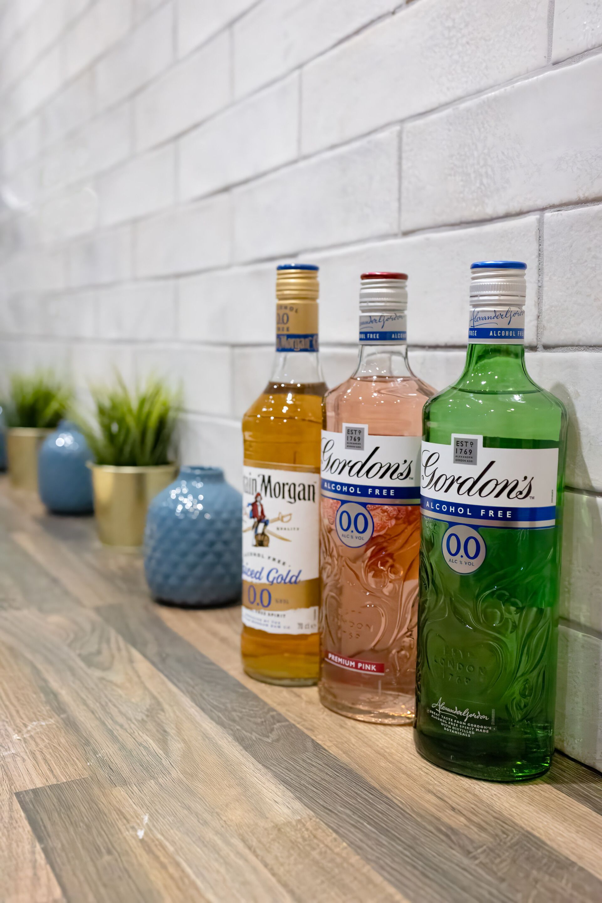 Three bottles of Gordon's alcohol-free spirits on a wooden shelf against a white brick wall.