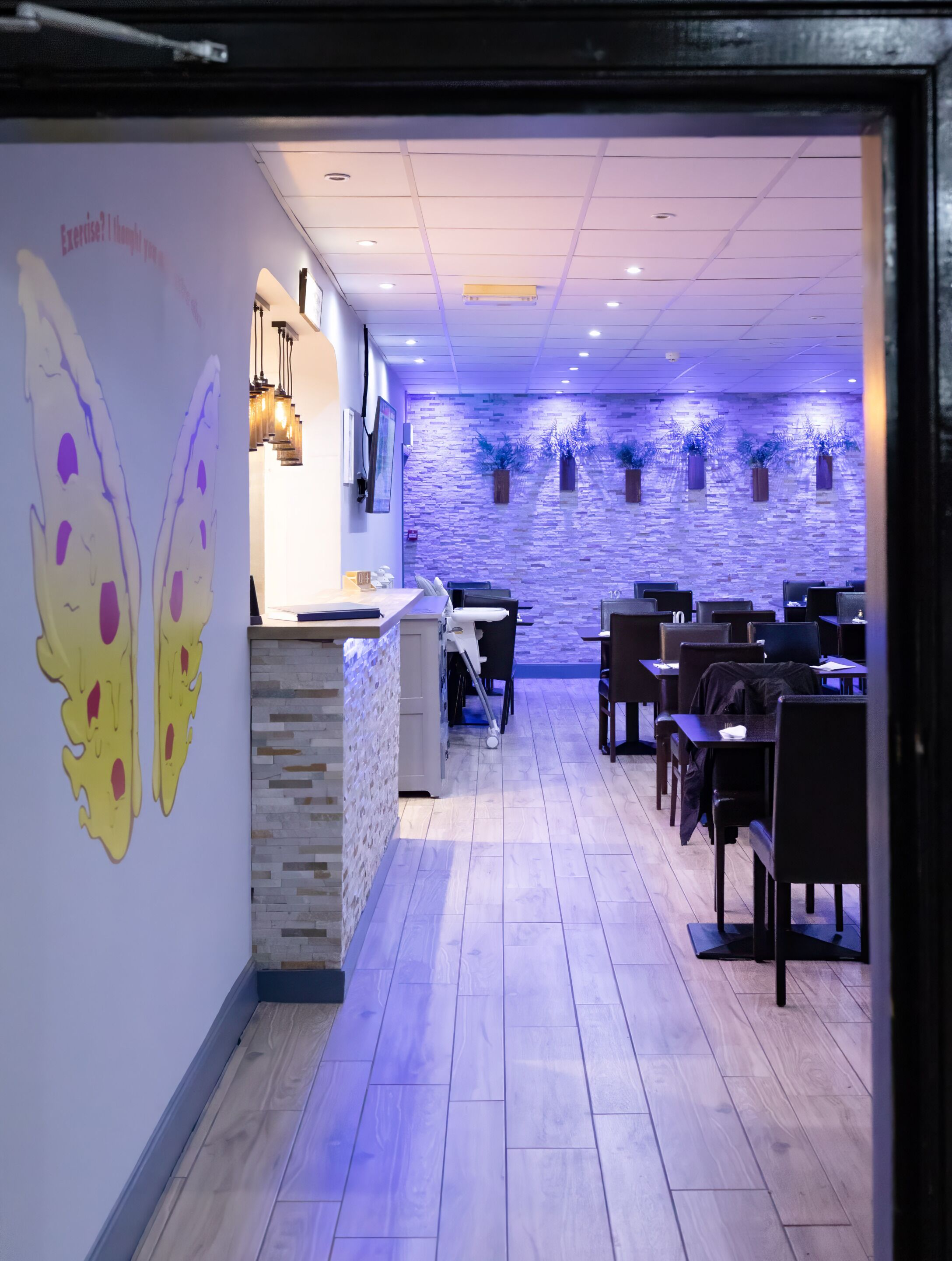 A restaurant interior with a long counter, multiple tables, and a decorative wall with a butterfly mural.
