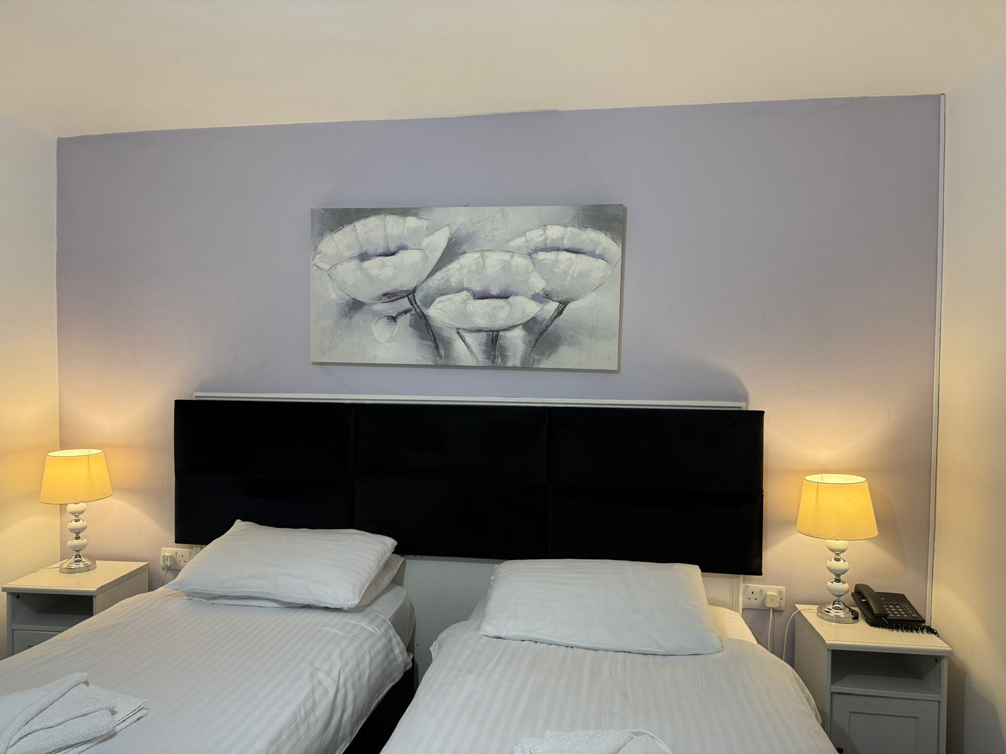 Ein Hotelzimmer mit zwei Einzelbetten, einem großen abstrakten Gemälde an der Wand und Nachttischlampen.