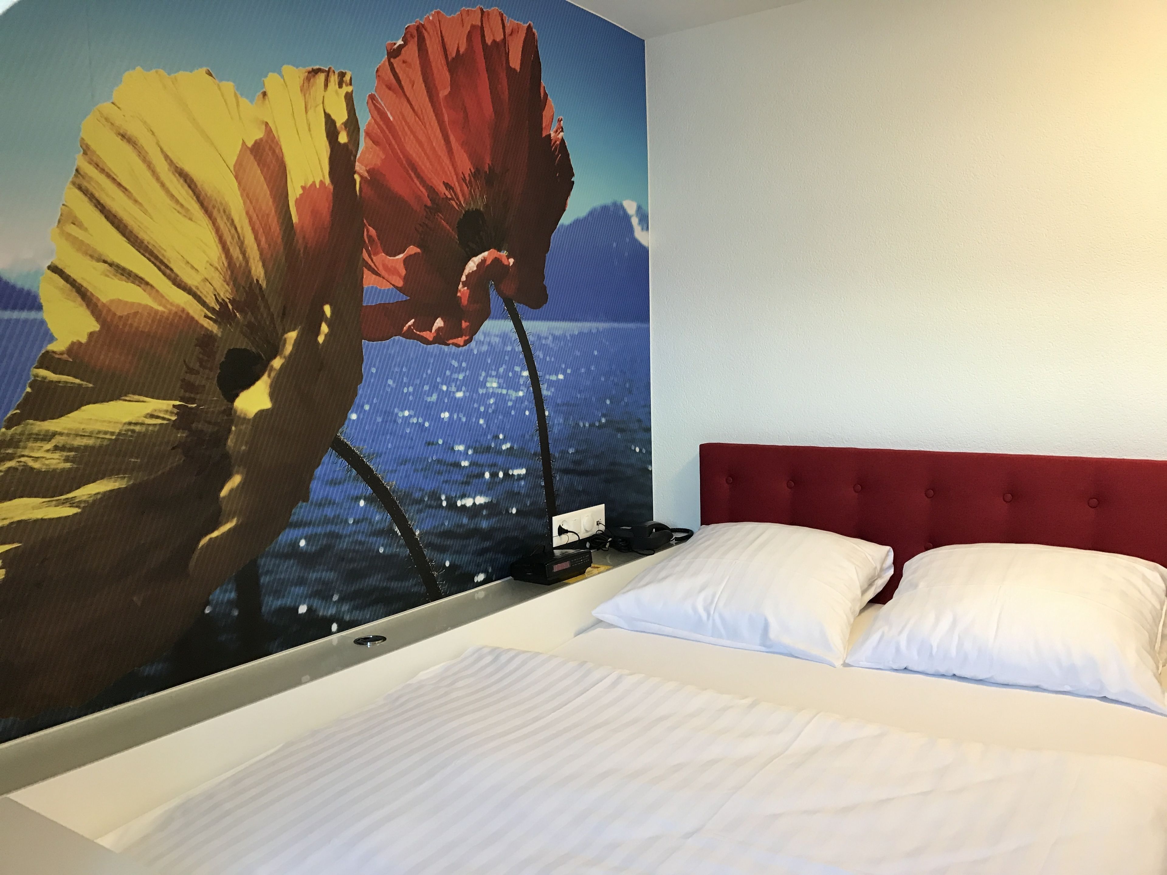 Una habitación de hotel con una cama grande, cabecera roja y un mural de flores en la pared.