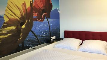 Una habitación de hotel con una cama grande, cabecera roja y un mural de flores en la pared.