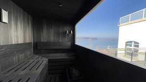 Una habitación moderna y minimalista con un amplio ventanal que ofrece vistas al mar y colinas lejanas.
