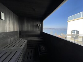 A modern, minimalist room with a large window offering a view of the sea and distant hills.