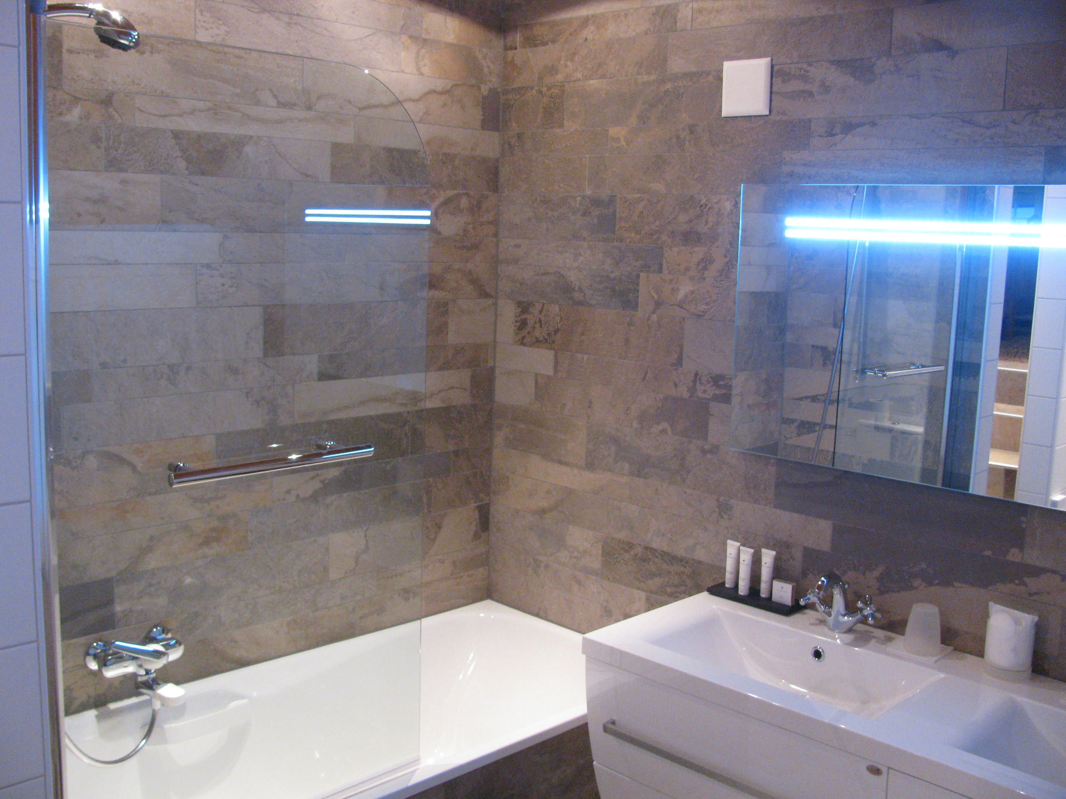 A modern bathroom with a glass-enclosed shower, a white bathtub, and a vanity with a mirror.