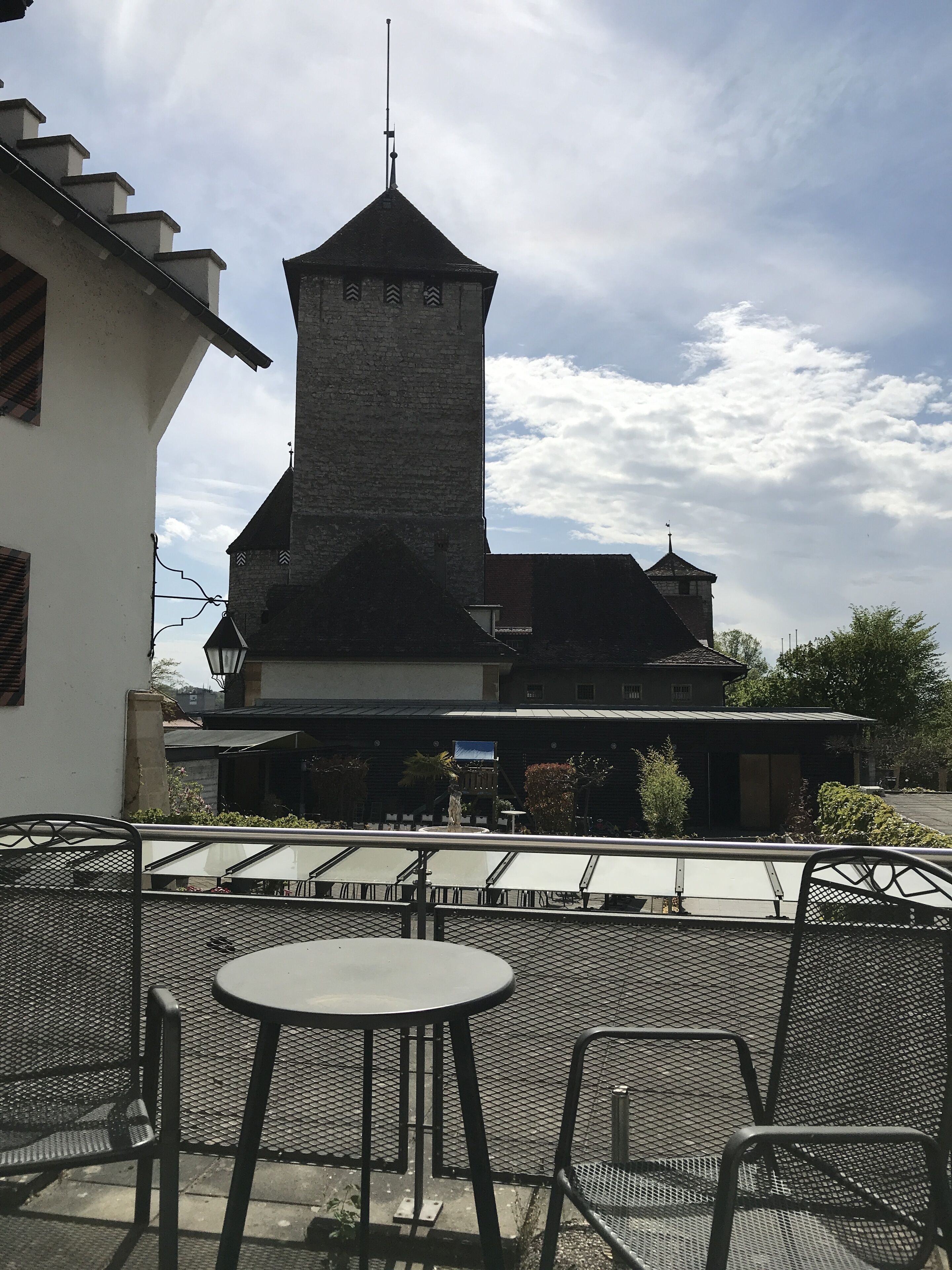 An outdoor seating area with tables and chairs, a building with a tower, and a clear sky.